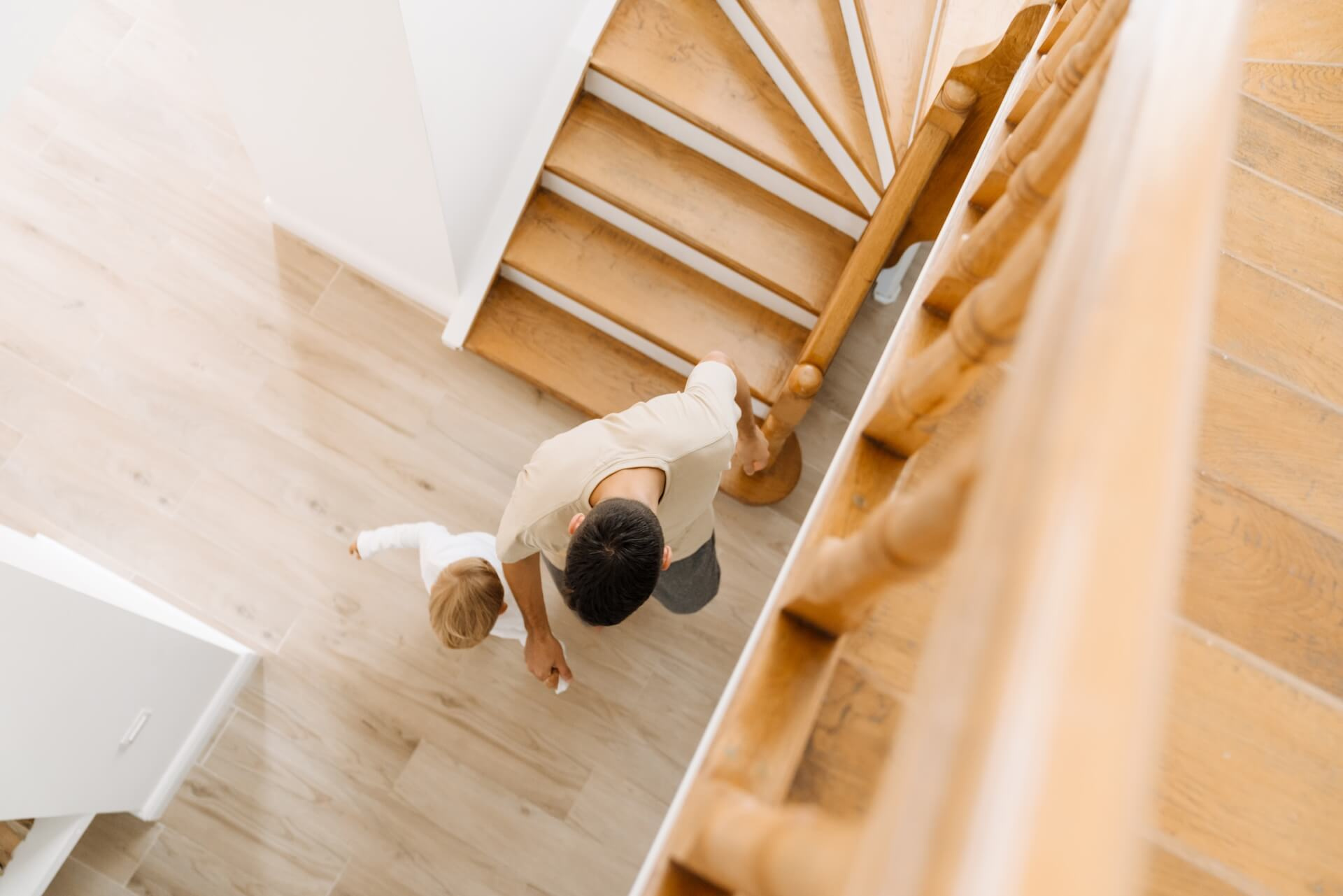A father and a small child walk up a beautiful wooden spiral staircase, showing the beautiful result of a staircase renovation.